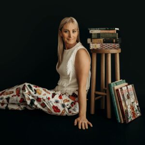 Chef Deb leans against a stool with an assortment of vintage cookbooks