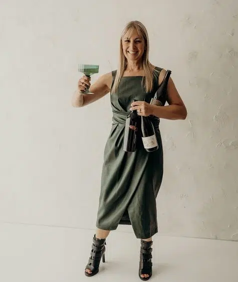 Chef Deb in green dress welcoming with wine bottles in hands