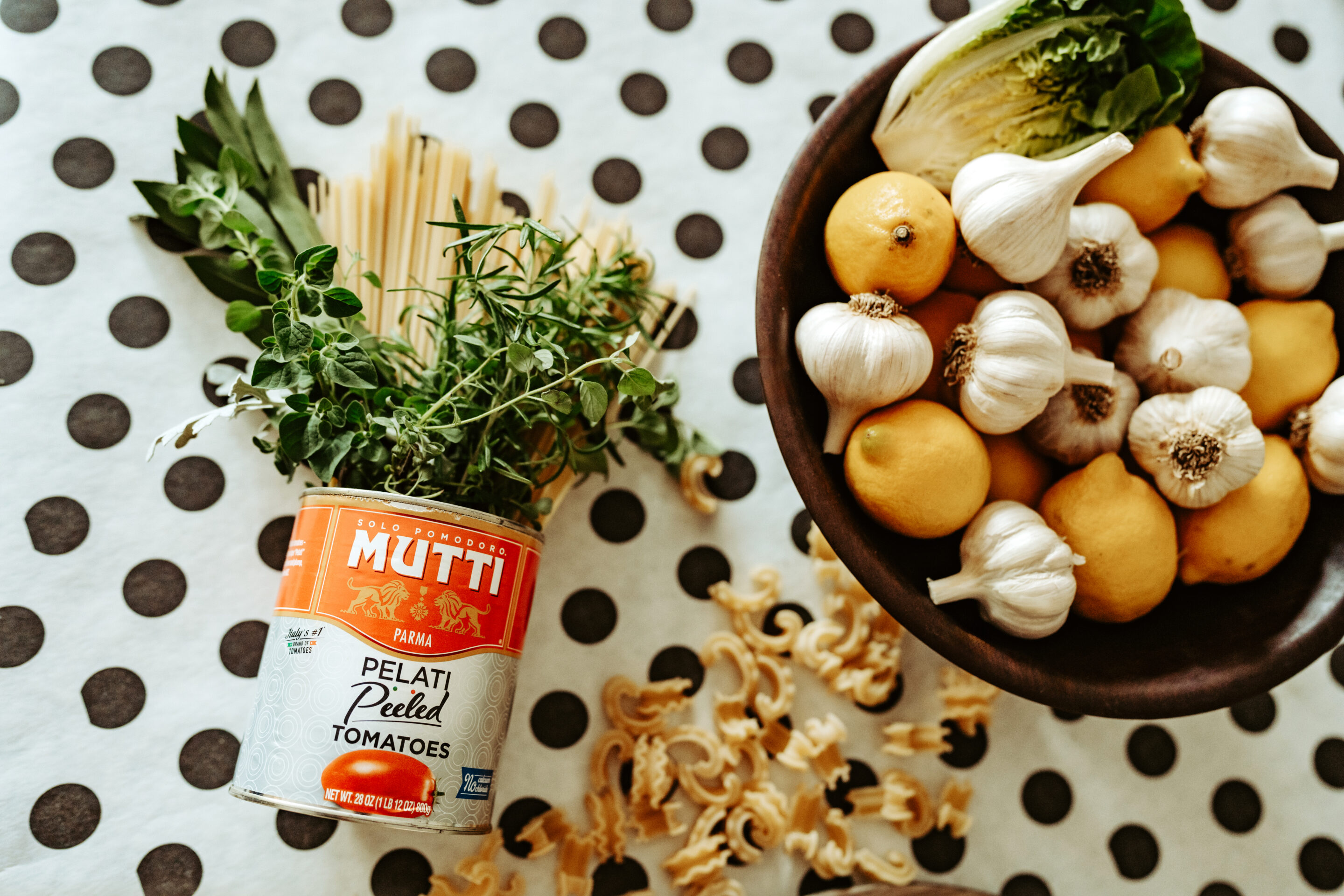 image shows dried pasta and herb floral arrangement with bowl of garlic and lemons alongside